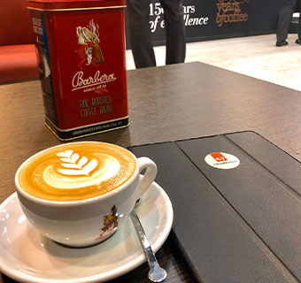 Cappuccino mit Latte Art Motiv, im Hintergrund Metalldose mit Barbera Logo