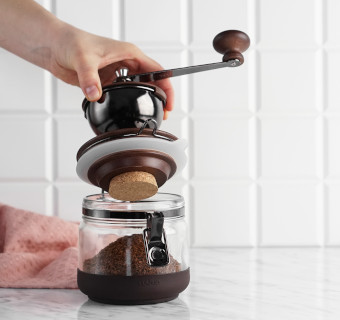 Mit Kaffeemehl gefüllte Hario Handmühle Canister vor weißem Hintergrund