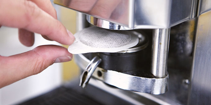Hand legt Kaffeepad in Maschine ein 
