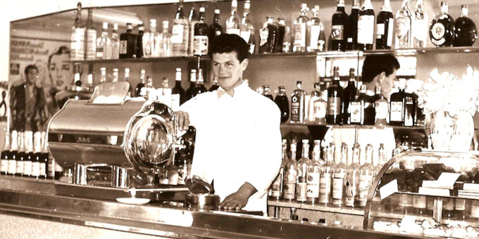 Schwarz-weiß Aufnahme mit Person hinter einer Bar vor einer Kaffeemaschine