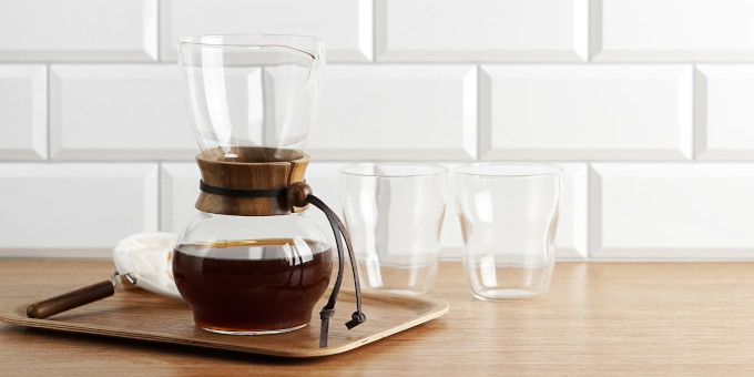 Karaffe mit Kaffee auf einem Tablett, dahinter zwei Gläser vor weißer Wand