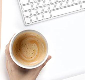 Eine Hand hält eine Tasse mit Kaffee vor einer Tastatur