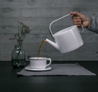 Kaffee wird aus einer Kaffeekanne in eine Tasse gekipppt