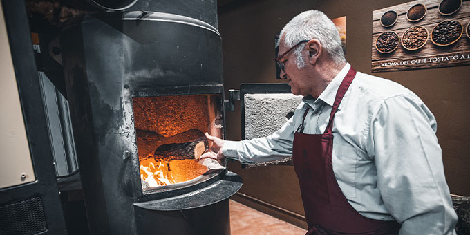 Mann legt Holzstück in einen brennenden Ofen