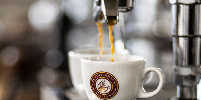 Zwei weiße Porzellantassen mit De Koffiemann Logo die vom Siebträger mit Espresso befüllt werden